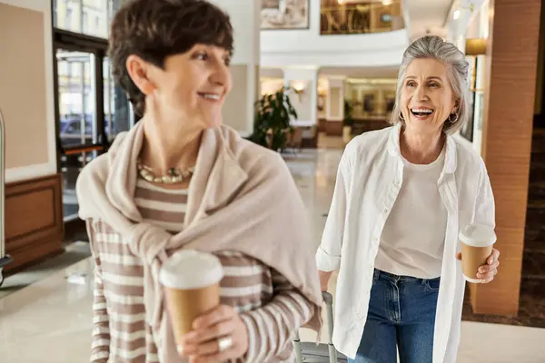 Dos mujeres disfrutando de un paseo por un centro comercial mientras sostienen tazas de café. - foto de stock