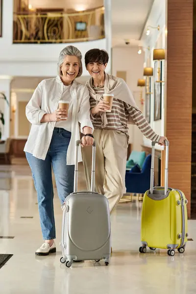A senior lesbian couple walks down a hallway with luggage. — Stock Photo