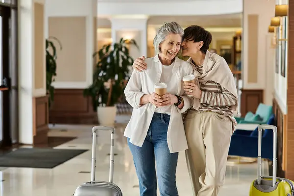 Deux amants lesbiennes seniors debout ensemble dans un hôtel, partageant un moment tendre. — Photo de stock