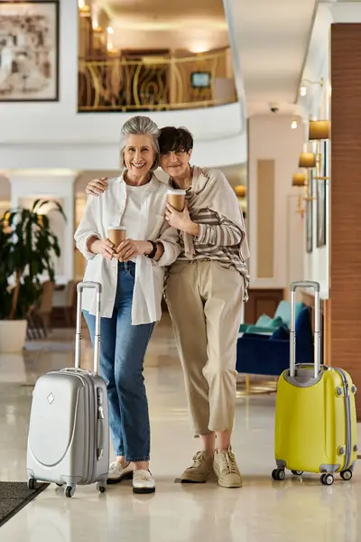 Coppia lesbica anziana, una coppia lesbica anziana amorevole, si trova nella hall di un hotel con i bagagli. — Foto stock
