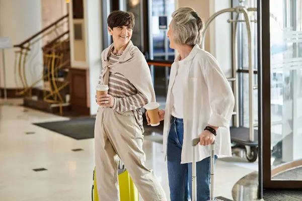 Loving senior lesbian couple standing with luggage in elegant hotel lobby. — Stock Photo