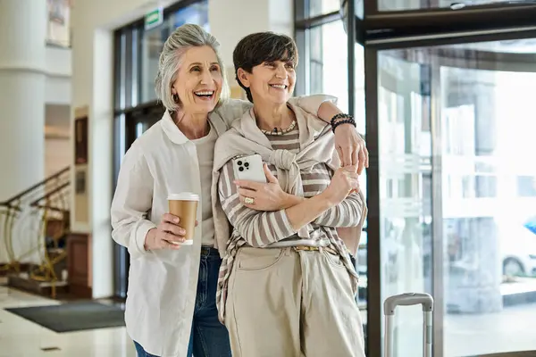 Two senior lesbian women stand outside a hotel, radiating elegance and love. — Stock Photo