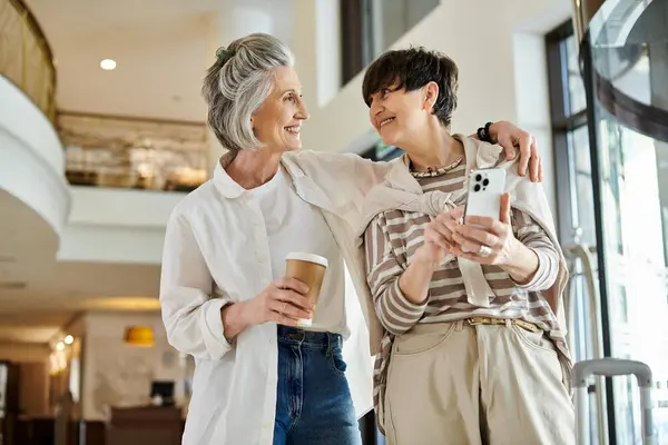 Two women, a senior lesbian couple, standing side by side holding coffee cups. — Stock Photo