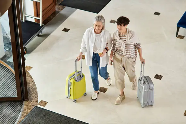 Amare anziani coppia lesbica passeggiando lungo il corridoio dell'hotel con i bagagli. — Foto stock