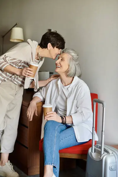 Senior lesbian couple spending time with love and tenderness while seated in a chair. — Stock Photo