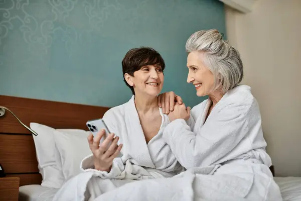 Un couple lesbien sénior en peignoir assis sur un lit, montrant amour et tendresse. — Photo de stock