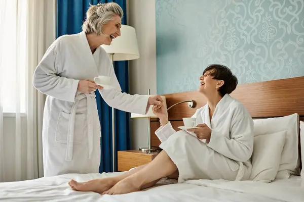 Senior lesbian couple cozying up with coffee in bathrobes - foto de stock