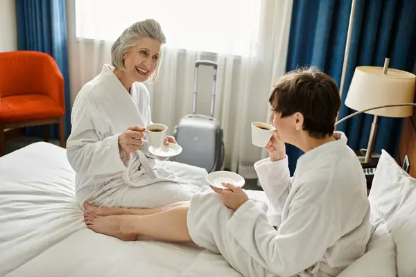 Senior coppia lesbica seduta vicino insieme sulla cima di un letto accogliente, condividendo un momento di tenerezza. — Foto stock