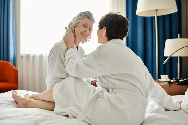Una mujer vestida de blanco se sienta en una cama junto a su pareja en un momento conmovedor. - foto de stock
