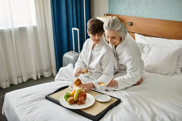 A loving senior lesbian couple, sitting on a bed, sharing a tender moment. - foto de stock