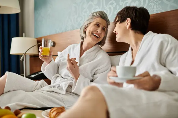 Two older women peacefully sitting on a bed in an intimate embrace. — Stock Photo
