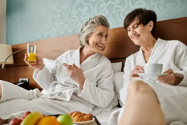 Ein zartes älteres lesbisches Paar genießt einen friedlichen Moment, während es auf einem bequemen Bett sitzt. — Stockfoto