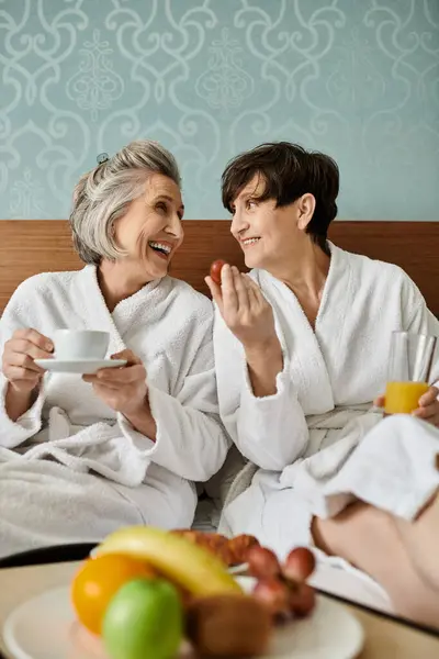 Two senior lesbian women sitting comfortably on a bed. - foto de stock