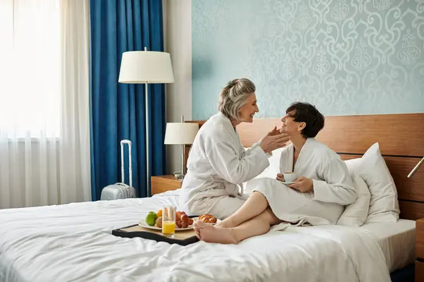 Two senior women, a loving lesbian couple, sit peacefully on top of a bed. — Stock Photo