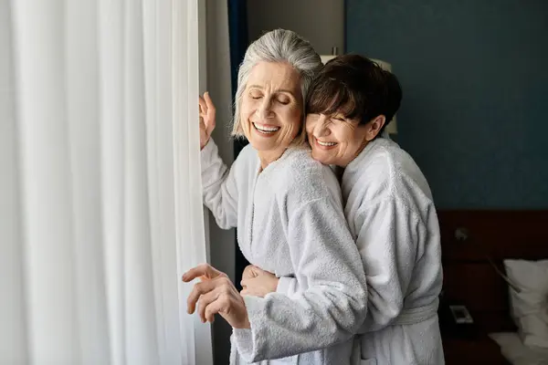 Deux lesbiennes âgées partagent un câlin tendre devant une fenêtre. — Photo de stock