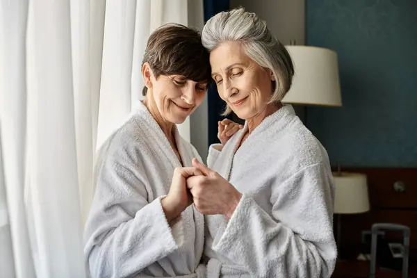 A loving senior lesbian couple wearing robes, together. — Stock Photo