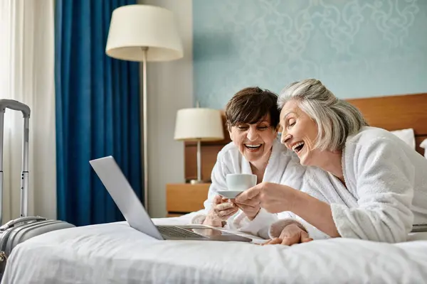 Senior lesbian couple sits on a bed, focused on a laptop screen. — Stock Photo
