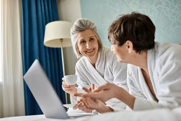 Una pareja de lesbianas mayores compartiendo una conversación en una acogedora habitación de hotel. - foto de stock
