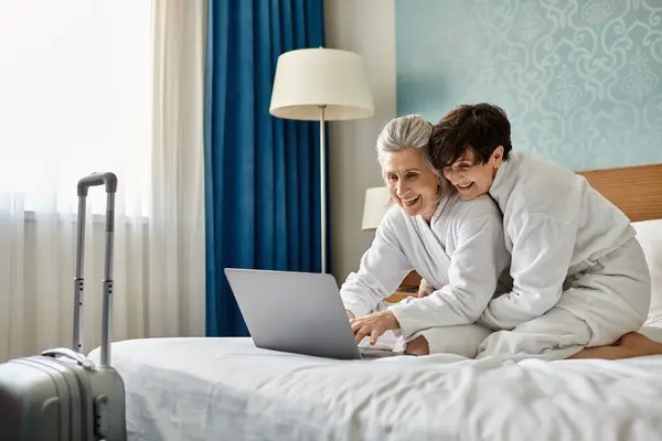 Senior lesbian couple share a laptop on a bed in a cozy moment. — Stock Photo