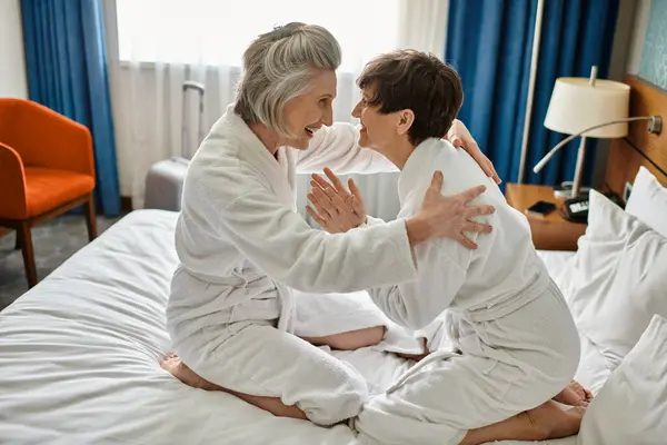 Deux femmes âgées profitant d'un moment tendre, assises sur un lit luxueux dans un hôtel. — Photo de stock