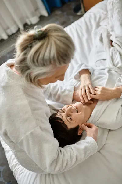Two senior lesbian women lay on a cozy bed in a tender embrace. — Stock Photo