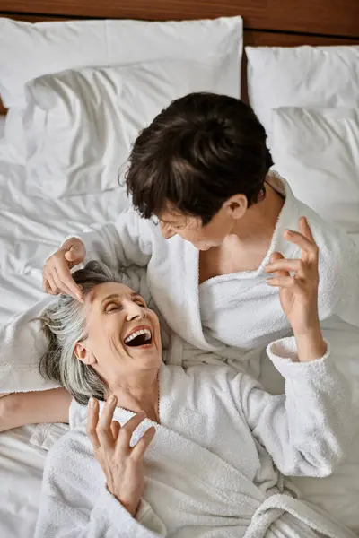 Senior lesbian couple embrace lovingly while laying in bed. - foto de stock