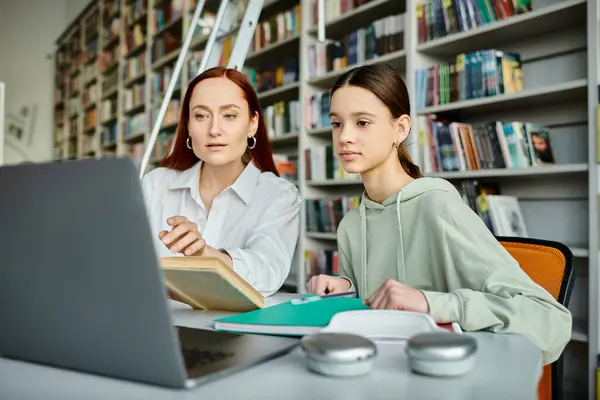 Un tutor rossa insegna a una ragazza adolescente in una biblioteca, utilizzando un computer portatile per le lezioni post-scolastiche. — Foto stock