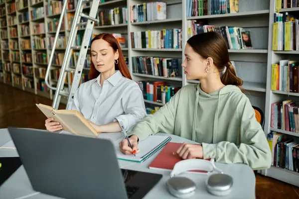 Un tutor rossa educa una ragazza adolescente in una biblioteca, utilizzando un computer portatile per le lezioni post-scolastiche. — Foto stock