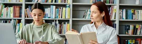 Un tutor con i capelli rossi insegna a un'adolescente in una biblioteca tra librerie alte, con un computer portatile aperto per l'educazione moderna. — Foto stock