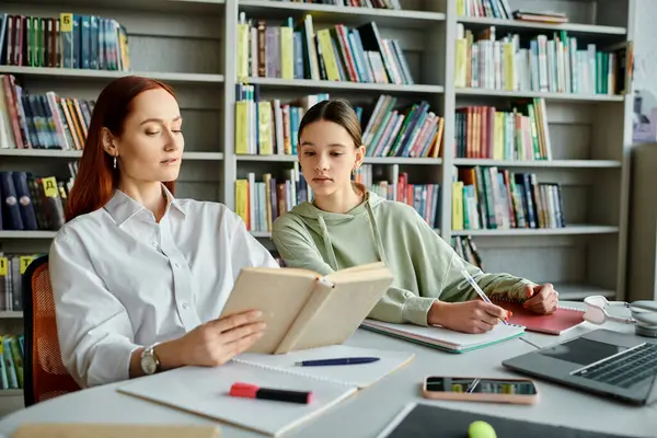 Un tutor con i capelli rossi sta insegnando a una ragazza adolescente a un tavolo in biblioteca, utilizzando un computer portatile per scopi educativi moderni.. — Foto stock