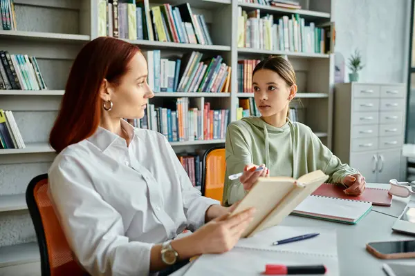 A redheaded tutor engages with a teenage girl in a library, using a laptop for after-school lessons in modern education. — Stock Photo