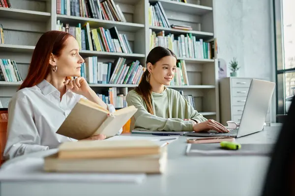 A redheaded tutor imparts knowledge to a teenage girl in a modern library setting, using a laptop for after-school studies. — Stock Photo