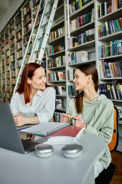Un tutor rossa sta insegnando una ragazza adolescente in una biblioteca, impegnandosi in lezioni post-scuola mentre si utilizza un computer portatile. — Foto stock