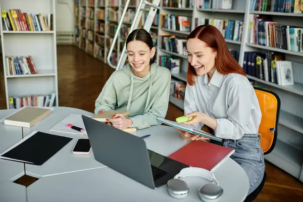 Un tutor dai capelli rossi insegna a un'adolescente in una biblioteca, impegnandosi in lezioni post-scolastiche con un computer portatile per l'educazione moderna.. — Foto stock