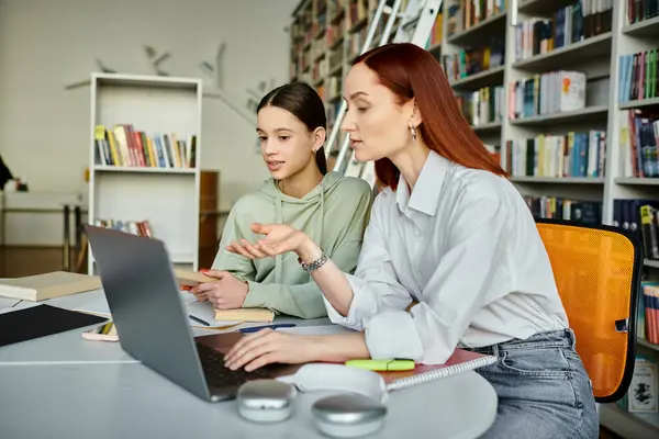 Un tutor con i capelli rossi guida un'adolescente durante una lezione post-scolastica utilizzando il computer portatile in un ambiente di biblioteca. — Foto stock
