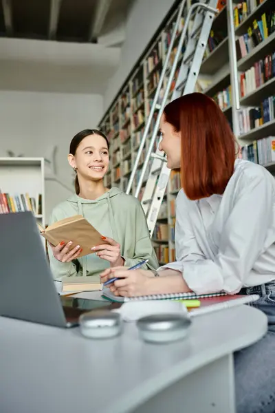 Un tutor dai capelli infuocati impartisce saggezza a un'adolescente tra gli scaffali rivestiti di libri e il bagliore di uno schermo portatile. — Foto stock