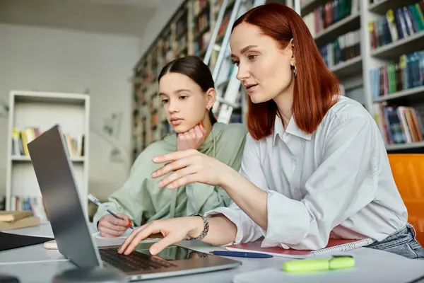 Redhead tutor and teenage girl engaged in after school lessons, utilizing a laptop for modern education in a library setting. — Stock Photo
