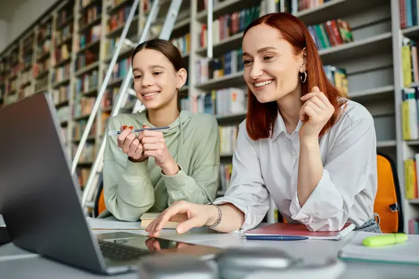 Un tuteur et son élève, travaillent avec diligence sur un ordinateur portable dans une bibliothèque, s'engageant dans des pratiques éducatives modernes. — Photo de stock