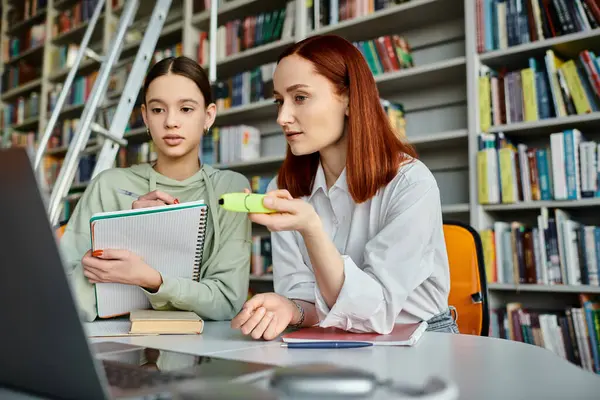 Teenage girl and tutor with red hair, engage in a modern education session in a library, focusing on a laptop screen. — Stock Photo