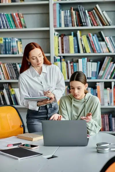 Tutor rossa e adolescente si impegnano nell'educazione moderna, discutendo le lezioni scolastiche su un computer portatile in un ambiente di biblioteca. — Foto stock
