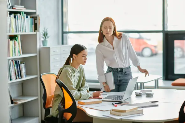 Un tutor rossa e un'adolescente lavorano insieme presso una scrivania in un ufficio, impegnandosi in lezioni post-scolastiche con l'aiuto di computer portatili.. — Foto stock