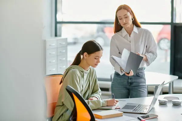 A redhead tutor and a teenage girl engage in after-school lessons at a desk, using a laptop for modern education. — Stock Photo