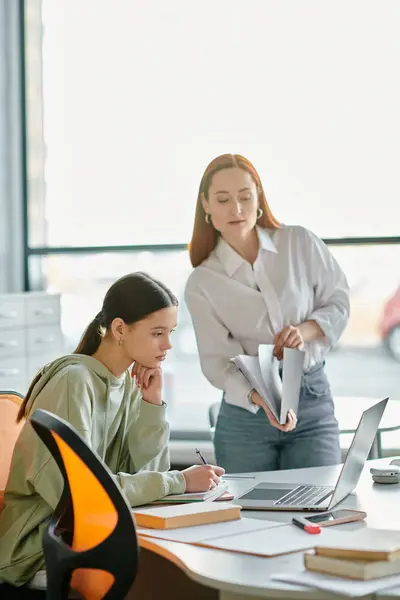 Un tutor rossa sta insegnando una ragazza adolescente a una scrivania in un ambiente ufficio, utilizzando un computer portatile per l'educazione moderna. — Foto stock