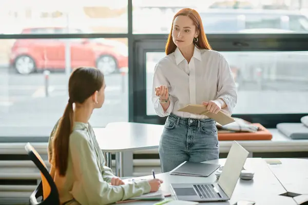 A redhead tutor teaches a teenage girl in an office setting, using a laptop for modern education after school. — Stock Photo