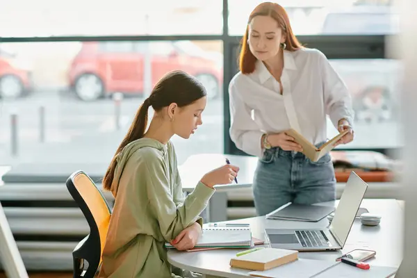 A redhead tutor is guiding a teenage girl in an office setting, utilizing a laptop for modern education. — Stock Photo