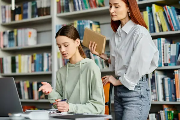 Un précepteur roux et un adolescent, engagés dans des leçons parascolaires dans une bibliothèque, à l'aide d'un ordinateur portable. — Photo de stock