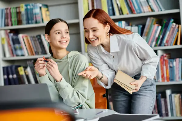 Un tutor rossa si impegna in una vivace discussione con una ragazza adolescente in una biblioteca, computer portatili aperti e menti desiderose. — Foto stock