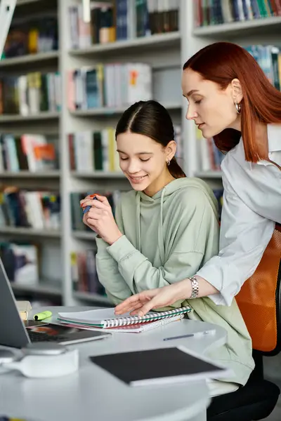A tutor with red hair teaches a teenage girl in a library, as they work together on a laptop for their modern education. — Stock Photo