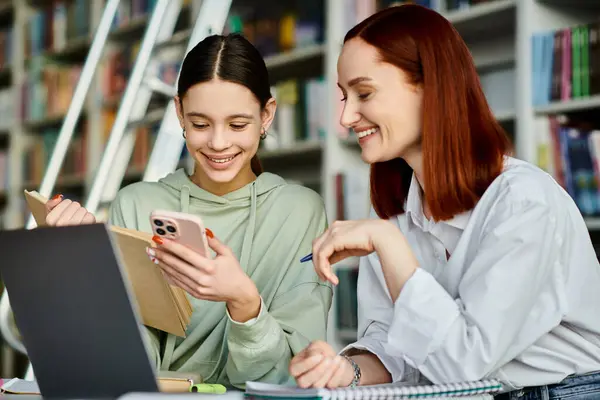 Tutor rossa guida una ragazza adolescente con lezioni post-scuola utilizzando un computer portatile in un ambiente accogliente biblioteca. — Foto stock