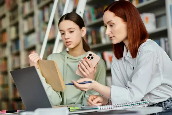 Un tutor con i capelli rossi insegna a una ragazza adolescente in una biblioteca, utilizzando un computer portatile per moderne risorse educative.. — Foto stock